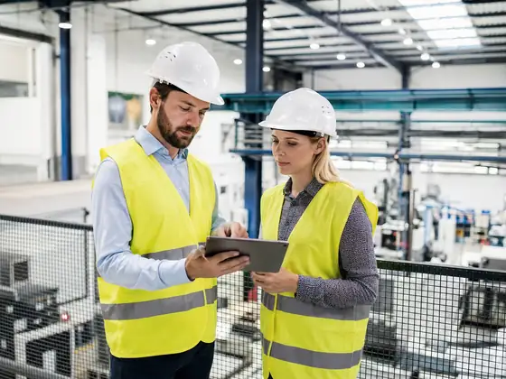 Fachkraft für Arbeitssicherheit im Gespräch mit einer Mitarbeiterin in einer Produktionshalle