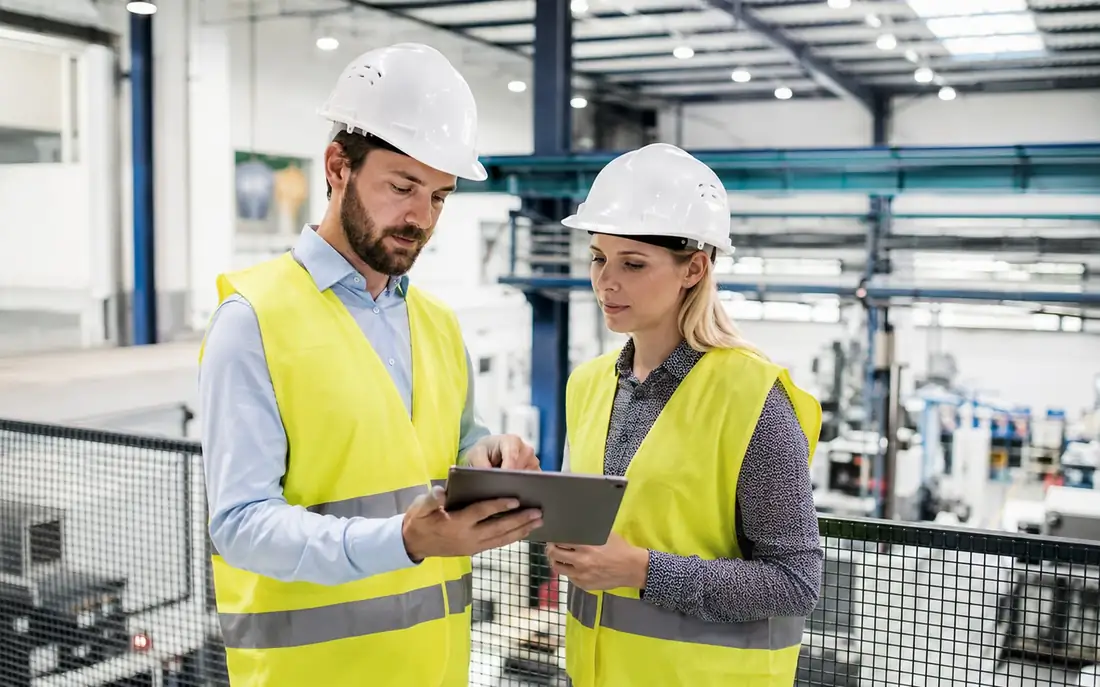 Sicherheitsfachkraft und Mitarbeiterin mit Warnwesten im Beratungsgespräch in einer Produktionshalle