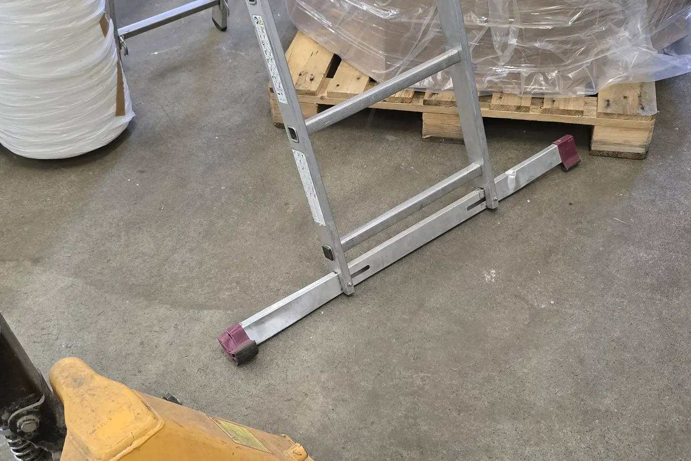 Unsicher zwischen Hubwagen und Palette aufgestellte Leiter