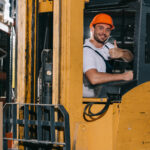 smiling warehouse worker showing thumb up and looking at camera while operating forklift loader